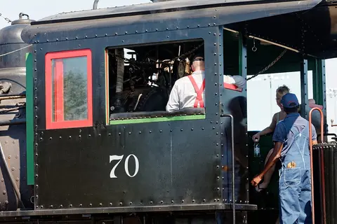 A steam train cab with people visible inside.