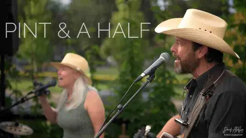 A musical duo performing outdoors with microphones and cowboy hats.