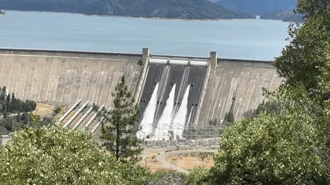 A large concrete dam releasing water through its spillways into a reservoir below.