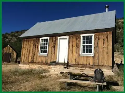 A wooden cabin with a metal roof stands outdoors under a blue sky.