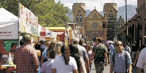 A crowded street market with food booths and a cathedral in the background.