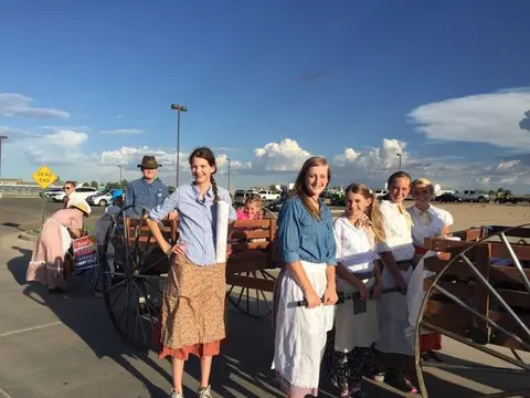 People in period costume pose next to a wagon outdoors.
