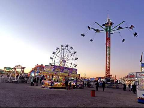 A carnival with various rides and food stands under an evening sky.