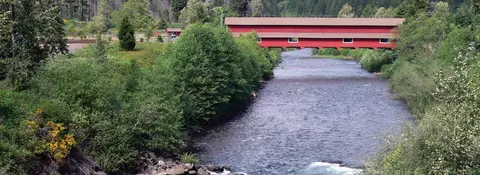 A red covered bridge crosses a river surrounded by trees.