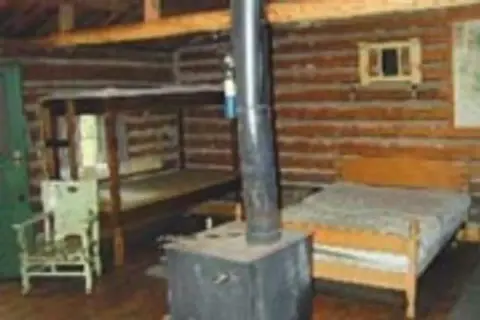 Interior of a rustic log cabin with beds and a stove.