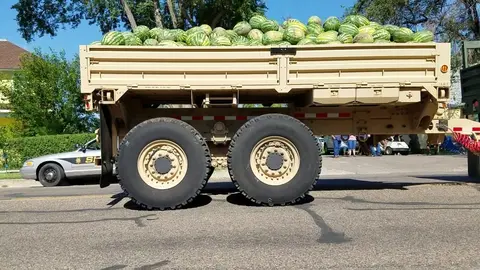 A large truck bed filled with numerous watermelons parked on a street.