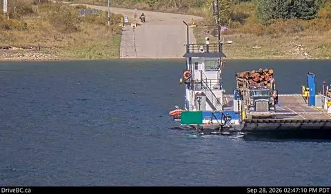 A ferry carrying a truck loaded with logs on the water.