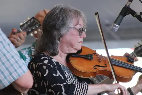 A woman plays the violin while performing with a band.