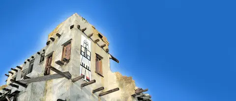 Exterior view of a historic building with wooden vigas and a painted figure against a clear blue sky.