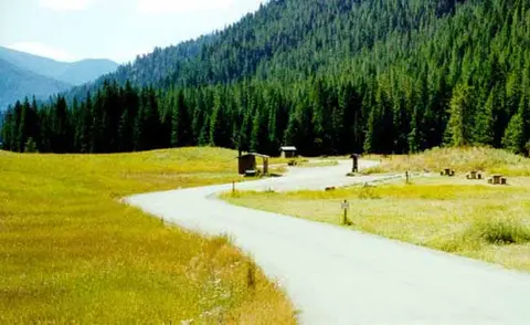 A winding road leads through a grassy valley toward a forested mountain.