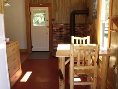 An interior view of a rustic room with a wooden table, chairs, and a stove.