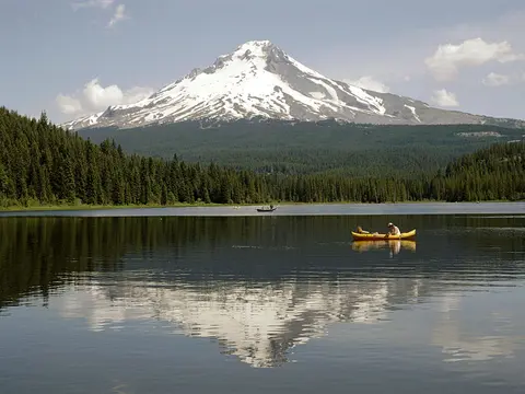 A scenic view of a snow-capped mountain reflecting in a lake with people canoeing.