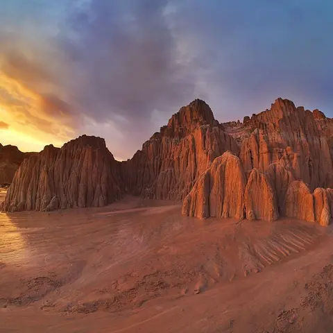 A landscape view of eroded rock formations under a dramatic cloudy sky at sunset.