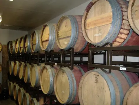Wooden wine barrels are stacked on metal racks inside a cellar.