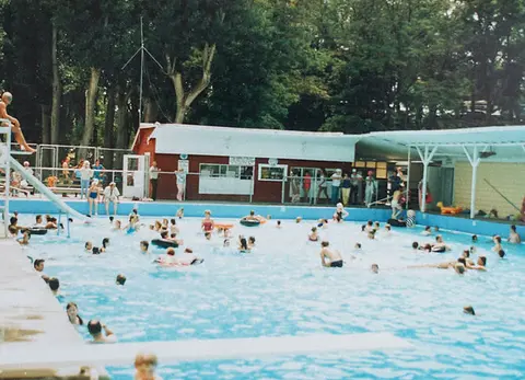 People enjoy swimming and relaxing in an outdoor pool on a sunny day.