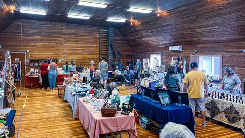 People browsing craft booths inside a large wood-paneled building.