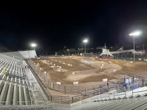 An illuminated dirt track arena with bleachers at night.