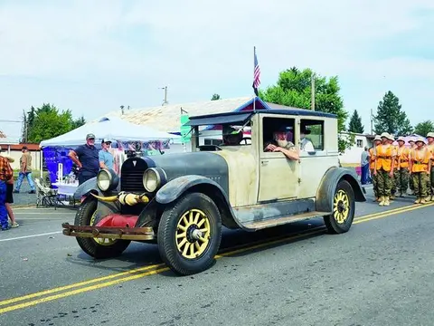 An old car drives down a street in a parade.