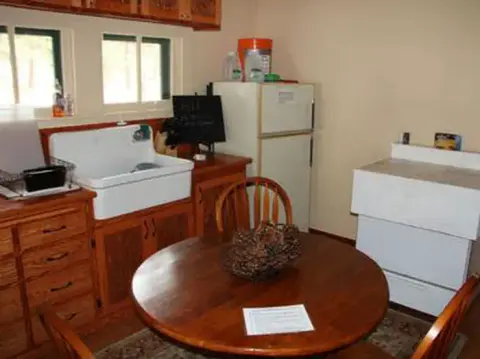 An interior view of a room with a round wooden table, sink, and refrigerator.