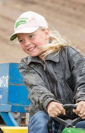 A child wearing a cap and jacket drives a small vehicle.