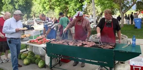 People grilling meat at an outdoor barbecue event.