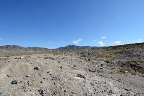 A dry landscape with sparse vegetation and distant mountains under a blue sky.