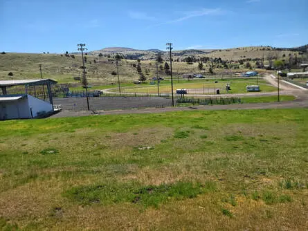A view of a grassy field, a running track, and low hills under a blue sky.