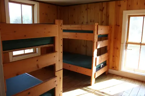 A room with wooden bunk beds and wood paneling on the walls.