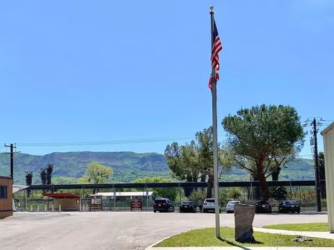An outdoor view showing a flagpole with an American flag, parked cars, and mountains in the distance.