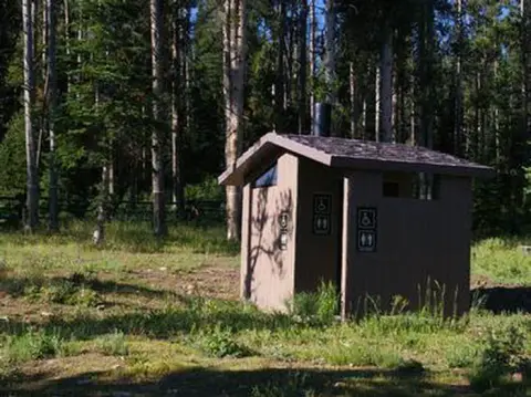 A small brown restroom building stands in a clearing surrounded by tall trees.