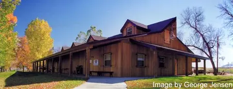 A long wooden building with a porch is surrounded by trees during autumn.