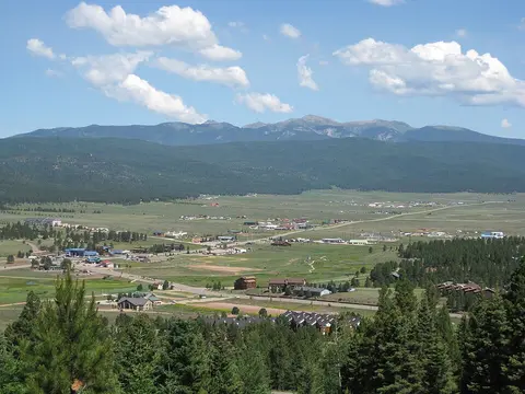 A scenic view of a valley town surrounded by forests and mountains under a blue sky with clouds.