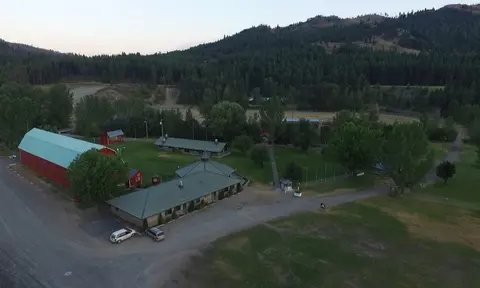 An aerial view of rural buildings nestled in a valley with forested mountains in the background.