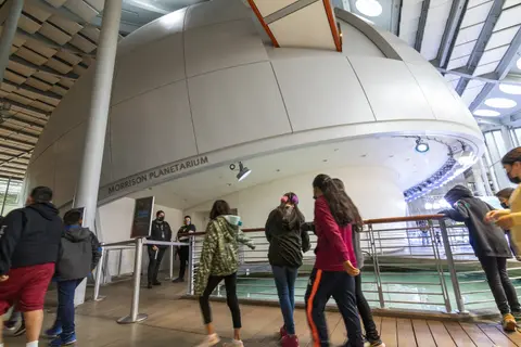 Visitors walk inside a building near a large planetarium dome.