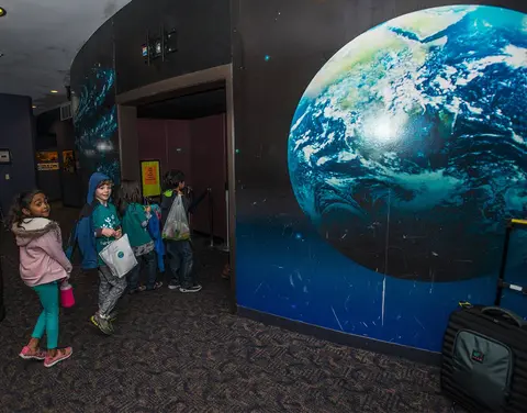Children walk down an indoor hallway decorated with a large mural of Earth.