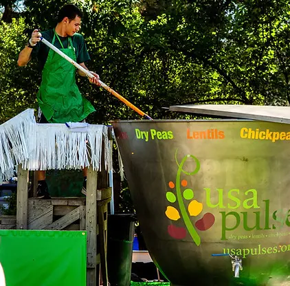 A person stirring a large metal container outdoors.