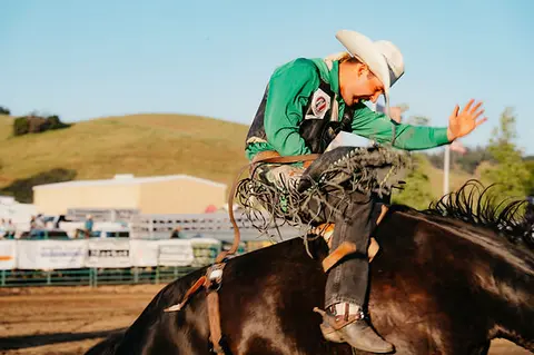 A cowboy rides a bucking horse at a rodeo.
