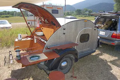 A small teardrop camper trailer parked outdoors with its rear galley hatch open.
