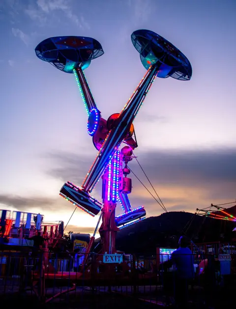 A brightly lit carnival ride stands against a twilight sky.