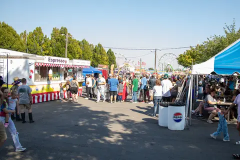 A busy outdoor carnival with food trucks and people walking around.