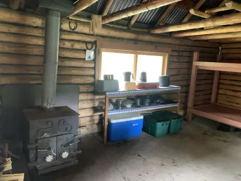 Interior of a rustic log cabin with a wood-burning stove and bunk beds.