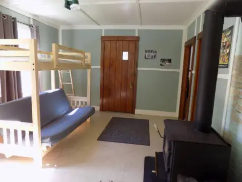 An interior view of a room with a bunk bed, couch, wood stove, and wooden doors.