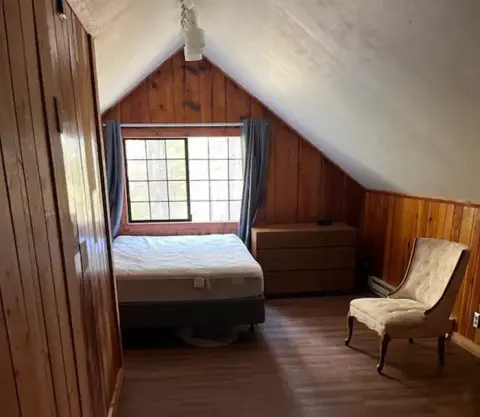 An attic bedroom with wood-paneled walls, a sloped ceiling, and a bed under a window.