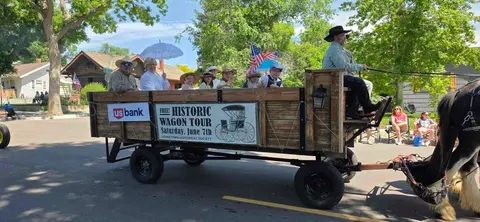 A horse-drawn wagon carries people in period clothing down a street.