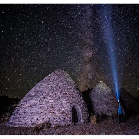 A person shines a flashlight near stone kilns under a starry night sky.