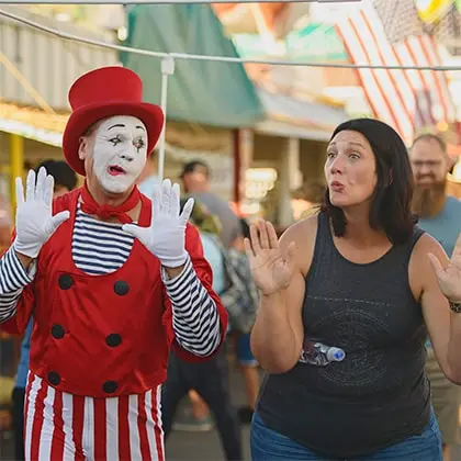 A mime in costume and a woman posing with their hands up outdoors.