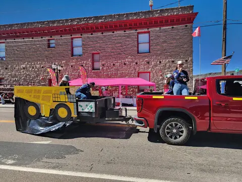 A red pickup truck pulls a decorated trailer in a parade.