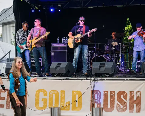A band performs on an outdoor stage with a woman dancing in the foreground.