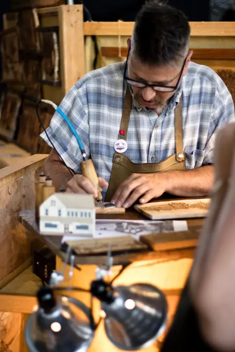 A man uses a wood burning tool at a wooden table.