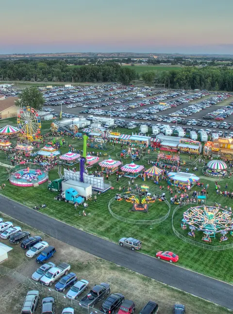 An aerial view of an outdoor carnival with rides, booths, and large parking lots.